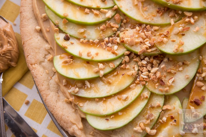 Taffy Apple Pizza // When you start with a sugar cookie crust, it's hard to go wrong. Add on a creamy layer of peanut butter and cream cheese. Top with sliced apples, caramel, and chopped nuts. This Taffy Apple Pizza will be the star of the party! | Tried and Tasty