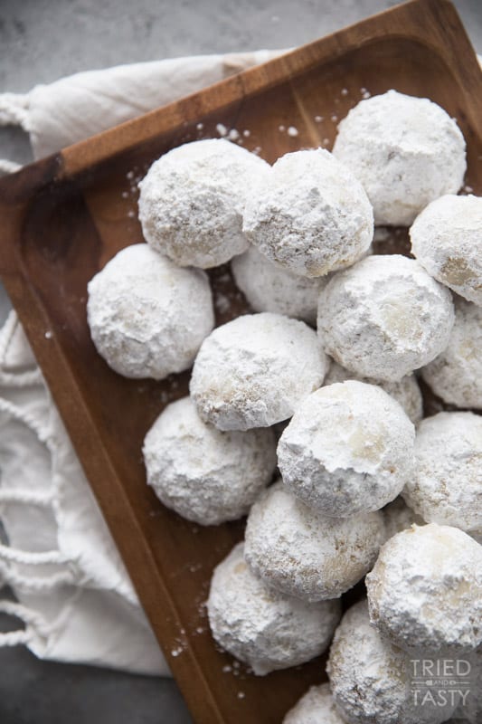 Stack of nut butterball cookies on a brown rectangular wooden plate resting on a dish towel