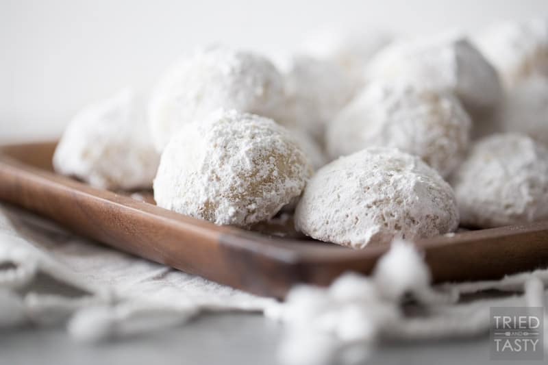 Stack of nut butterball cookies on a brown rectangular wooden plate resting on a dish towel