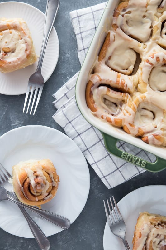 Three separate plates each with one cinnamon roll and a fork on a counter
