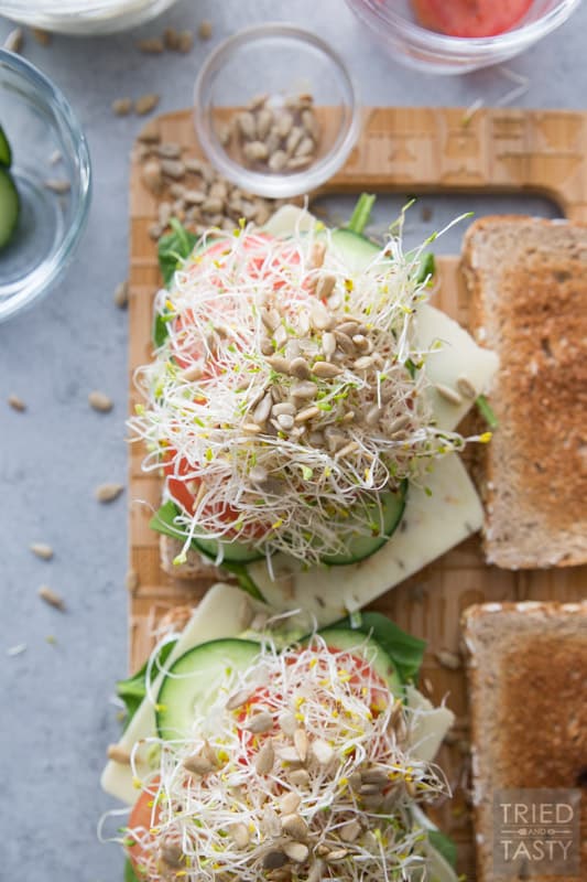 A close up image of an open face veggie sandwich topped with sprouts