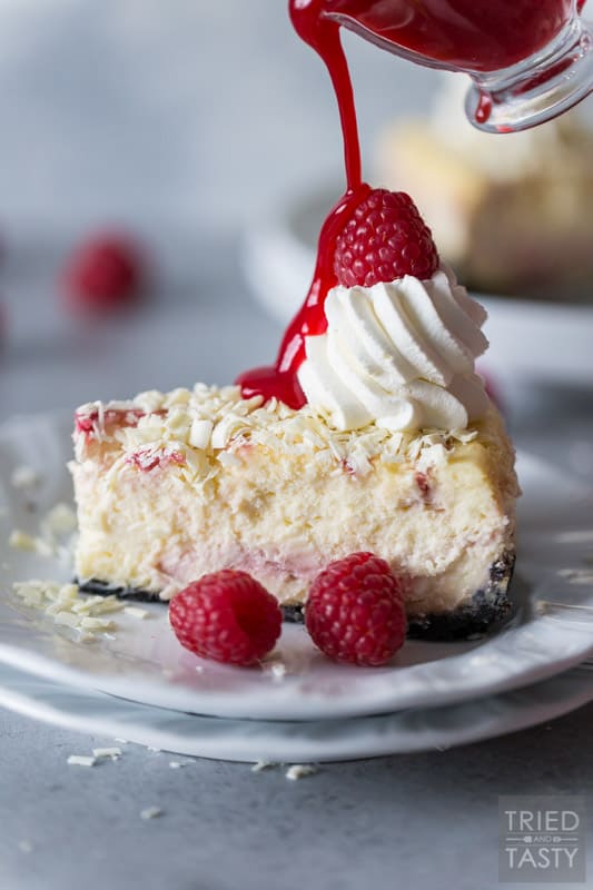 Raspberry sauce being drizzled on a slice of Cheesecake Factory White Chocolate Raspberry Truffle Cheesecake on a white plate