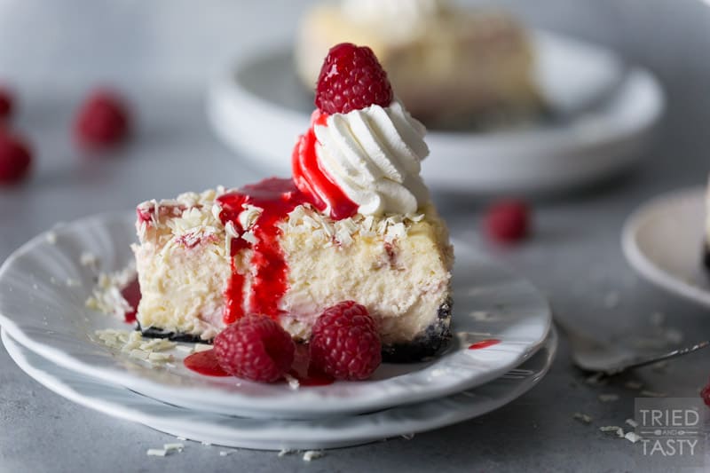 Raspberry sauce drizzled on a slice of Cheesecake Factory White Chocolate Raspberry Truffle Cheesecake on a white plate