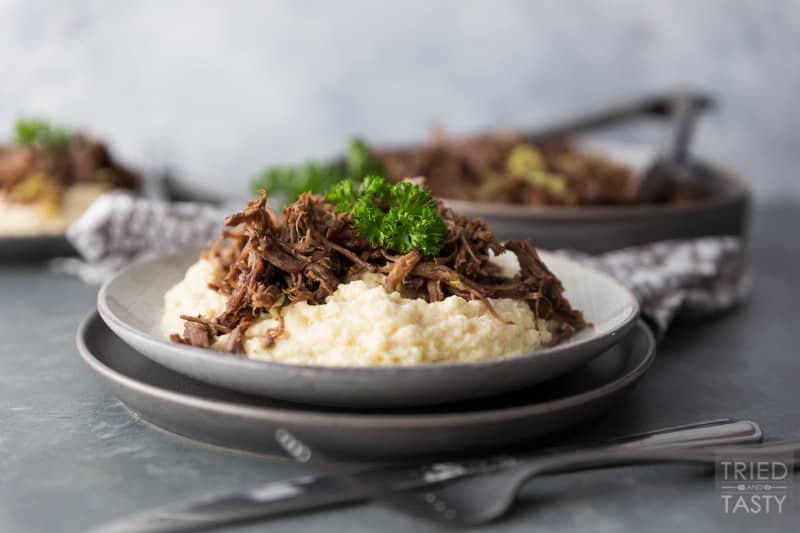 Two plates stacked with mashed cauliflower topped with shredded pot roast garnished with parsley