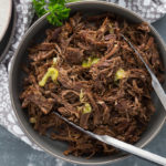 Bowl of shredded pot rot topped with a few pepperoncini pepper slices