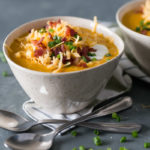 Sweet potato soup in a ceramic bowl topped with shredded cheddar, bacon, sour cream & scallions