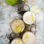 Several glasses of Green Apple Kombucha Slushy, with green apples and ice in the background.