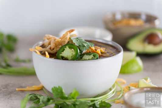 Bowl of chili garnished with jalapeños, tortilla strips and cheese.