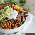 Barbacoa Beef Burrito Bowl with cheese, salsa, corn, lettuce, pinto beans, gaucamole, lime, cilantro & sour cream on top.
