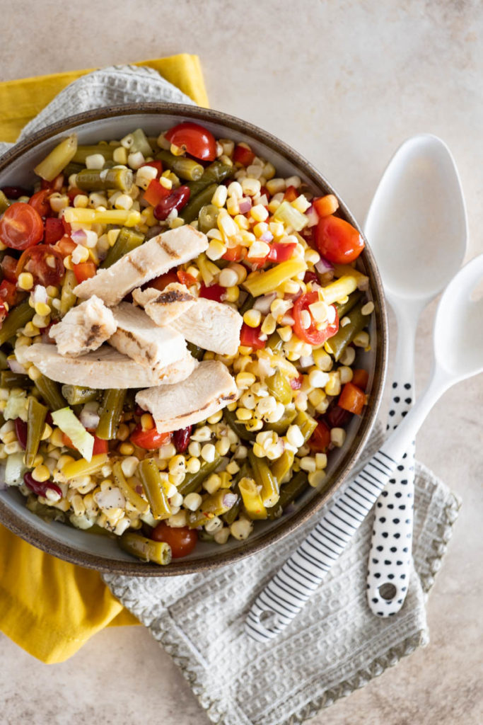 A prepared bowl of bean salad, topped with sliced grilled chicken breast.