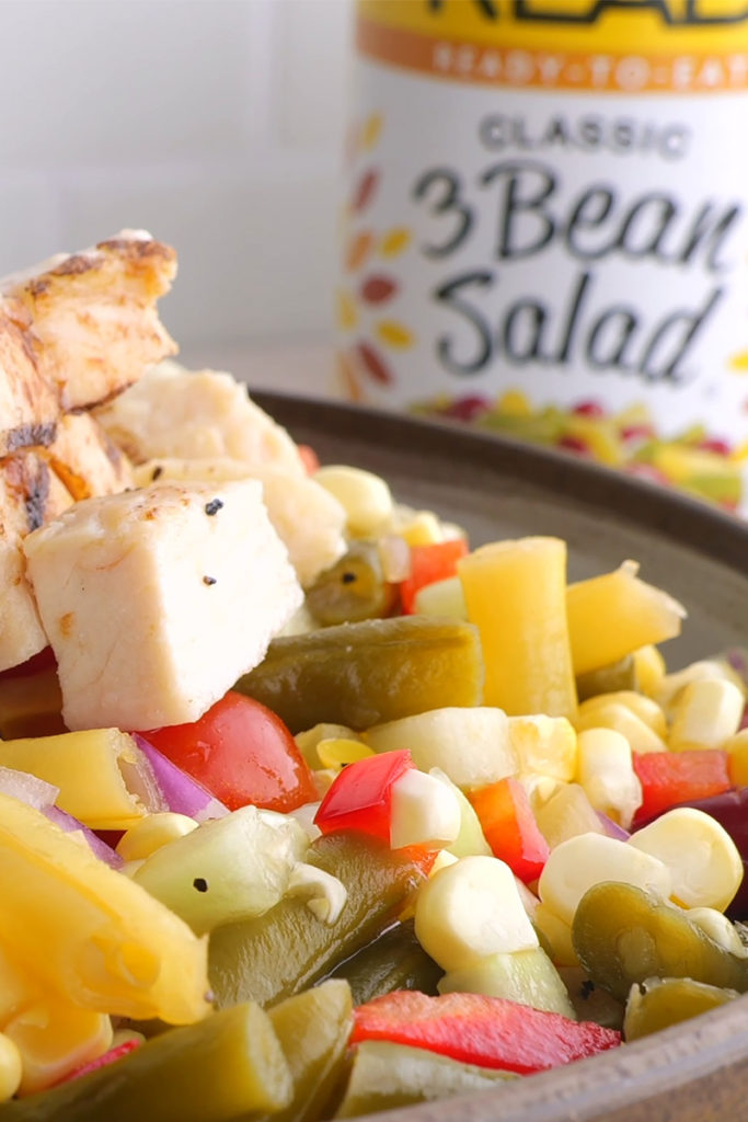A close up photo of the prepared Bean Salad in a brown bowl, with a can of READ 3 Bean Salad in soft focus in the background.
